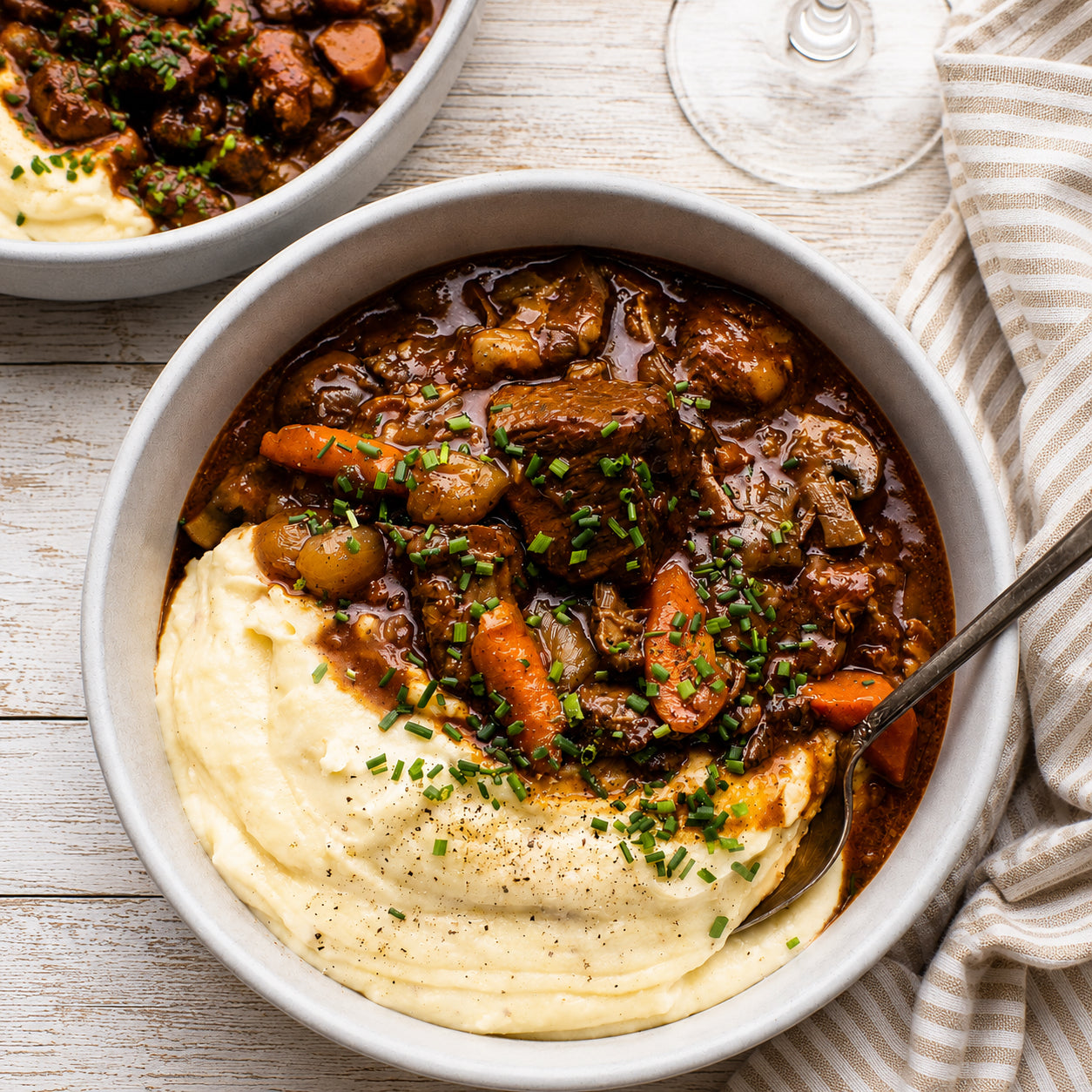 Bowl of beef bourguignon with mashed potatoes on a wooden table