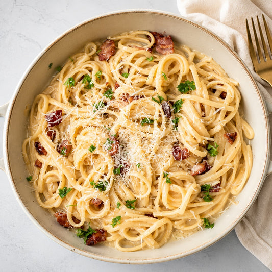 Spaghetti dish with bacon and herbs in a bowl on a light background