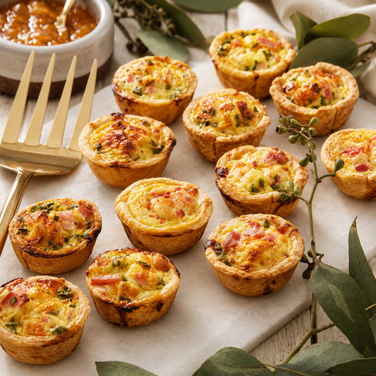 Mini quiches on a marble surface with a gold fork and small bowl of jam.