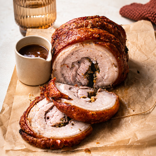 Sliced roasted pork roll with a side of sauce on brown paper