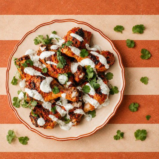 Tandoori Chicken pieces topped with white sauce and cilantro, served on a white plate with a red rim against a striped orange and beige background.