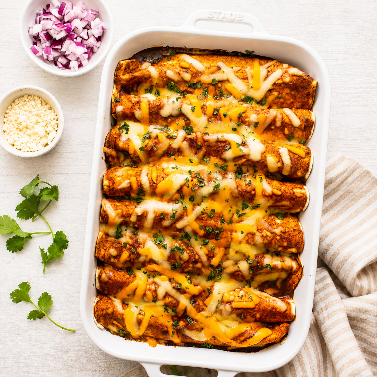 Baked enchiladas in a white dish with garnishes on a light background